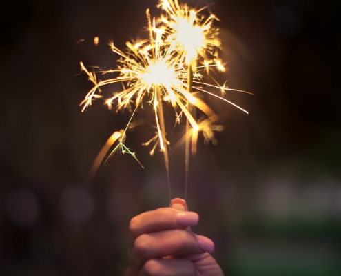 Woman holds sparklers against dark night background